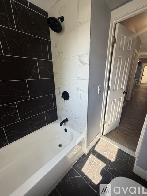 A bathroom with a black tiled shower area and a white bathtub.