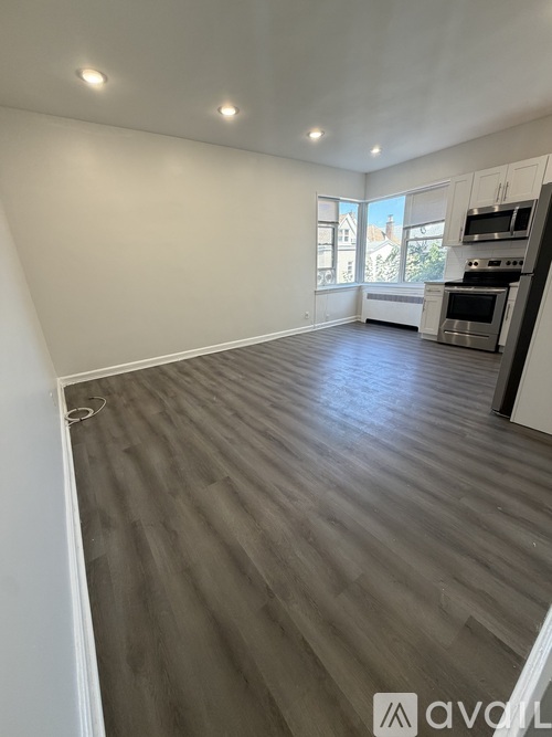 A spacious room with wooden flooring and a kitchen area in the background.