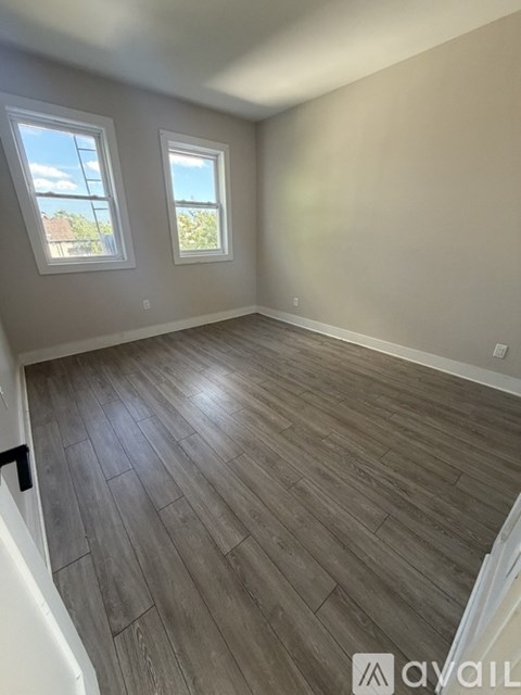 A room with wooden flooring and two windows.