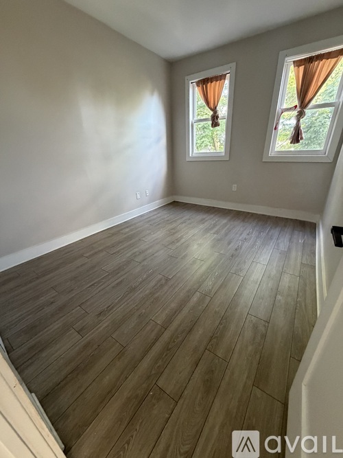 A room with wooden flooring and two windows with orange curtains.
