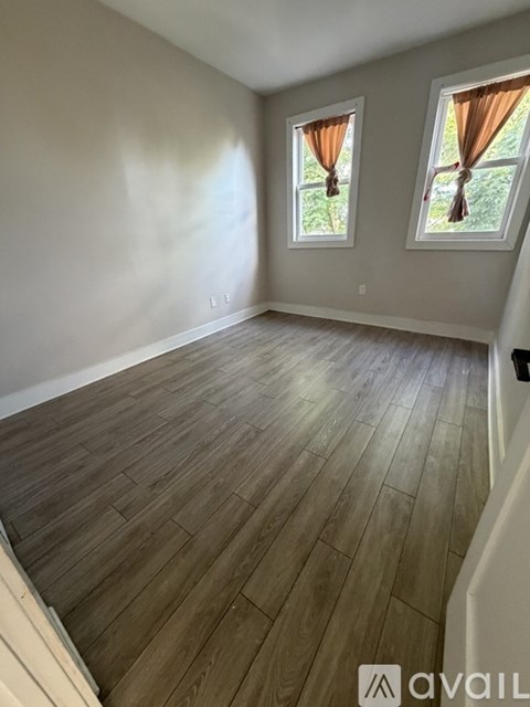 A room with wooden flooring and two windows with orange curtains.