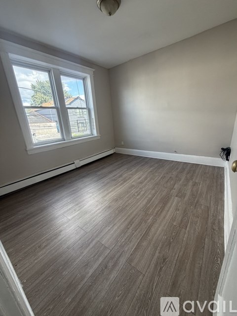 A room with wooden flooring and a window overlooking a residential area.
