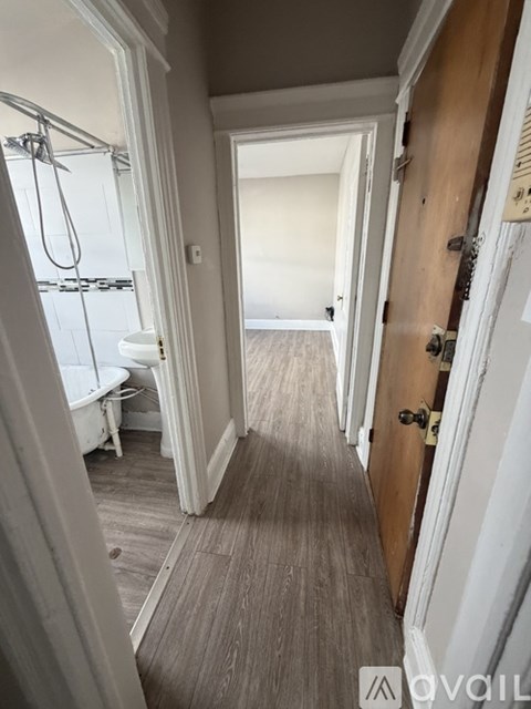 A narrow hallway with a door on the right and a window with a shower on the left.