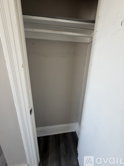 A white door is open to a small, empty room with a wooden floor.