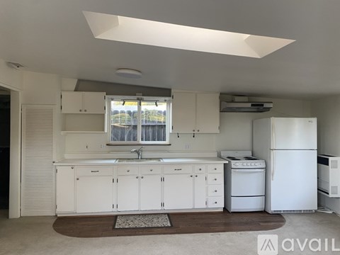 A kitchen with white cabinets and appliances, a window with a view of trees, and a rug on the floor.