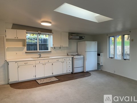 A kitchen with white cabinets and appliances, a rug on the floor, and a window with blinds.