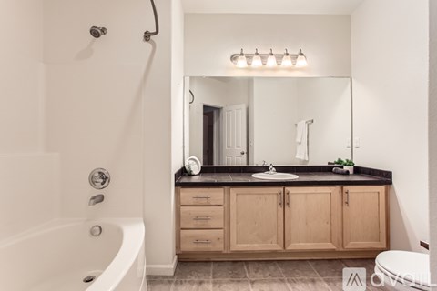 A bathroom with a white tub, sink, and wooden cabinets.