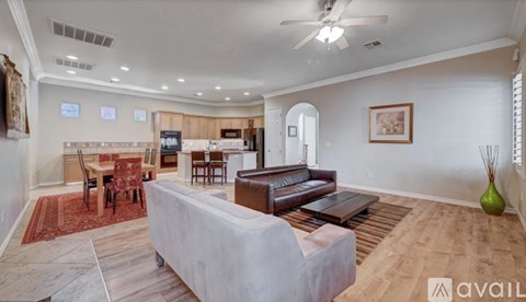 A spacious living room with a white sofa and a kitchen area in the background.