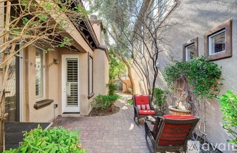 A patio with a red chair and a black bench is surrounded by plants and trees.