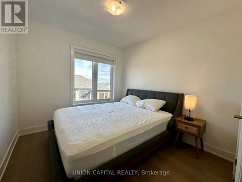 A bedroom with a large bed, a nightstand with a lamp, and a window with a view of the beach.