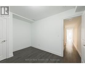 A spacious room with wooden flooring and white walls, with a door on the left and a hallway on the right.