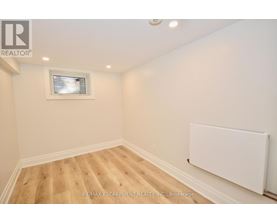 A room with wooden flooring and a white wall with a window.