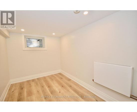 A room with wooden flooring and a white wall with a window.