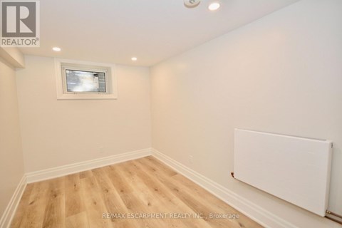 A room with wooden flooring and a white wall with a window.