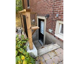 A wooden chair is leaning against a brick wall next to a door.