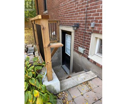 A wooden chair is leaning against a brick wall next to a door.