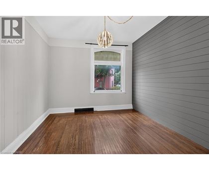 A room with wooden flooring and a window showing a red building outside.