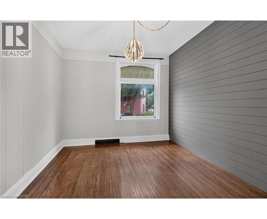 A room with wooden flooring and a window showing a red building outside.