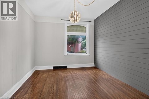 A room with wooden flooring and a window showing a red building outside.