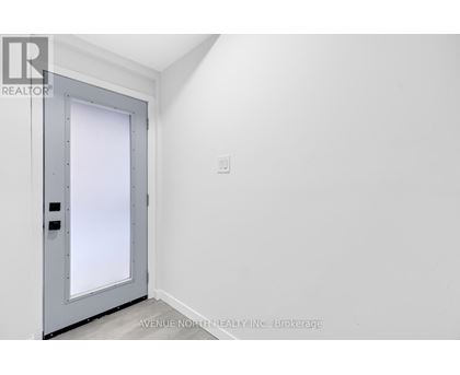 A grey door with a window in the middle is in a white room.
