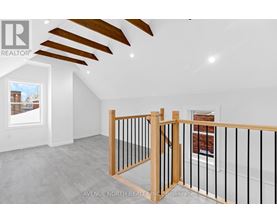 A real estate brokerage logo is displayed on a wall in an empty room with a wooden staircase and a window showing a view of a building outside.