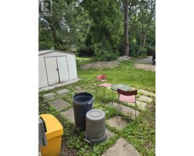 A backyard with a chair, table, and trash cans.