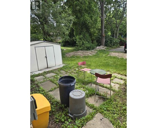 A backyard with a chair, table, and trash cans.