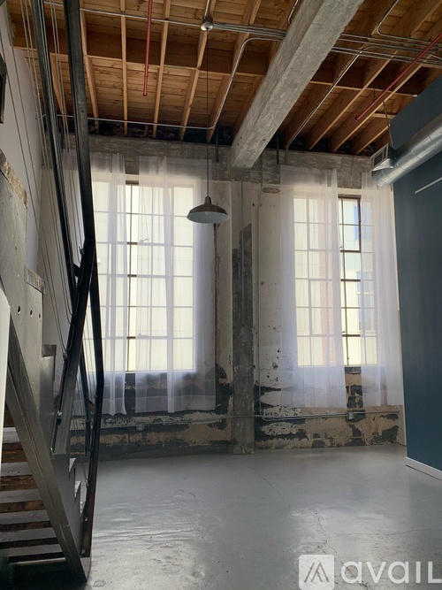 A large empty room with a staircase and two windows.