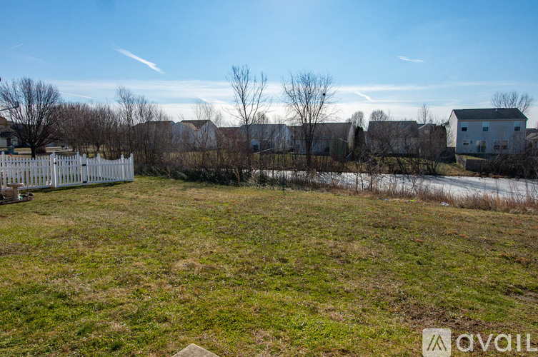 A grassy field with a white fence and houses in the background.