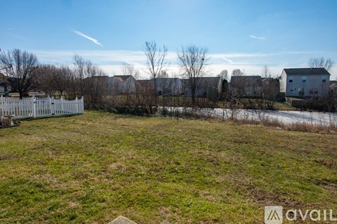 A grassy field with a white fence and houses in the background.