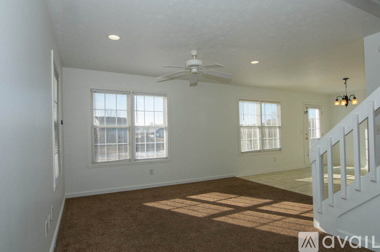 A spacious room with a carpeted floor, a ceiling fan, and a staircase.