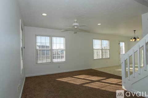 A spacious room with a carpeted floor, a ceiling fan, and a staircase.
