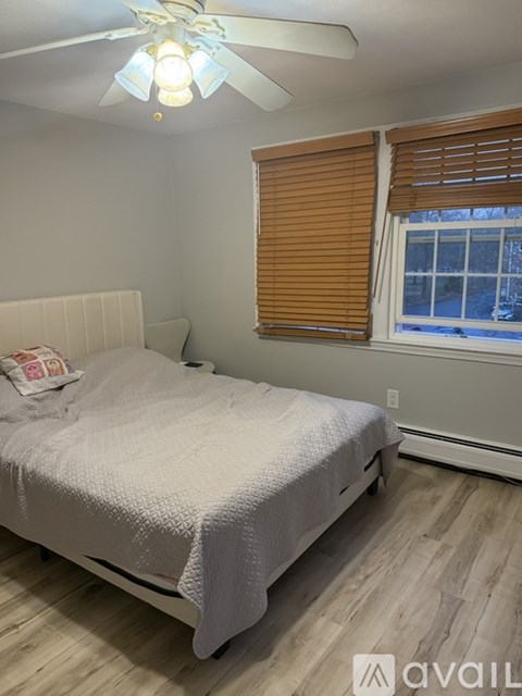 A bedroom with a bed, a window with blinds, and a ceiling fan.