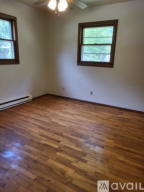 A room with wooden flooring and two windows.