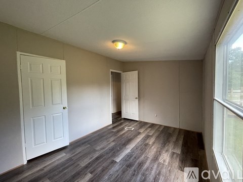 A room with a white door and a window with a view of trees outside.