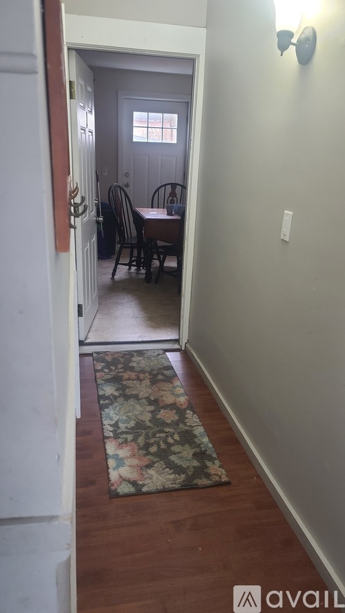 A hallway with a rug on the floor and a table and chairs in the background.