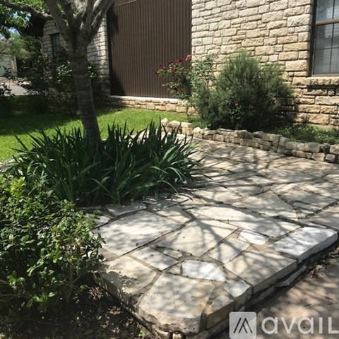 A stone patio with a tree and a house in the background.