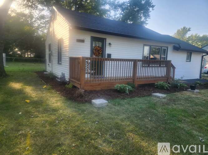 A small white house with a brown deck in the front yard.