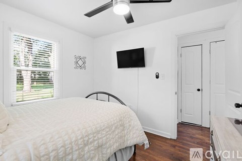 A bedroom with a bed, a ceiling fan, and a flat-screen TV mounted on the wall.