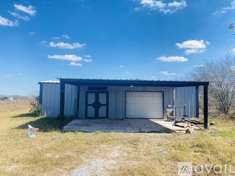 A large metal building with a garage door is situated in a grassy field.