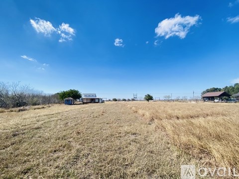 A field with a barn and a house in the distance under a blue sky.