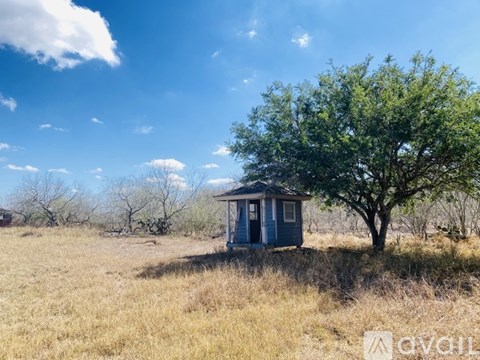 A small blue house sits in a field with a large tree in front of it.