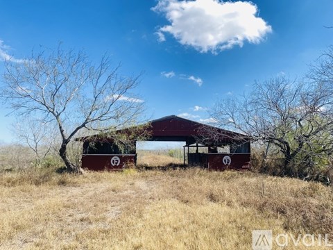 A red building with a white logo on it is situated in a field with dry grass and trees.