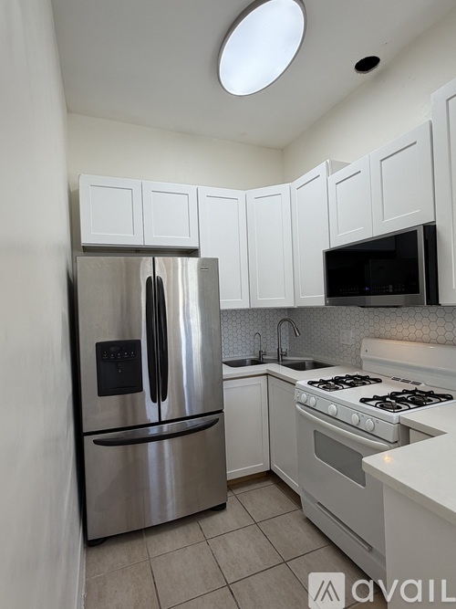 A kitchen with a stainless steel refrigerator, white cabinets, and a white stove top oven.