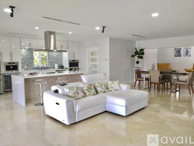 A modern living room with a white sofa and a kitchen area in the background.