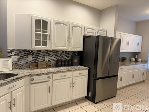 A kitchen with white cabinets and a black refrigerator.