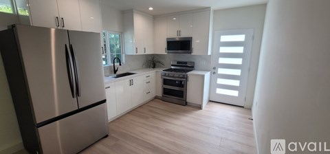 A modern kitchen with a stainless steel refrigerator and wooden flooring.