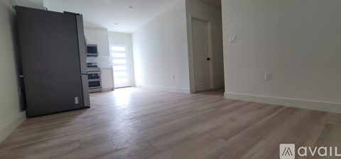 A spacious room with wooden flooring and a large refrigerator.