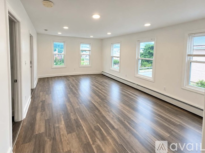 A spacious room with wooden flooring and three windows.