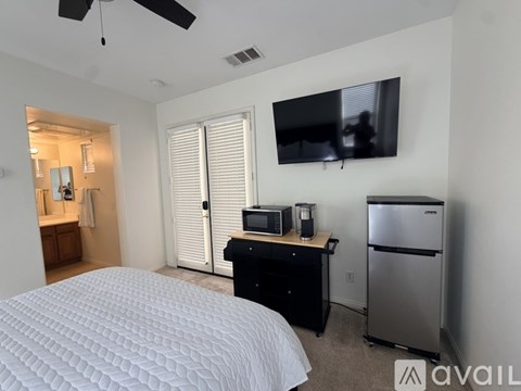 A bedroom with a bed, a TV, a microwave, and a refrigerator.